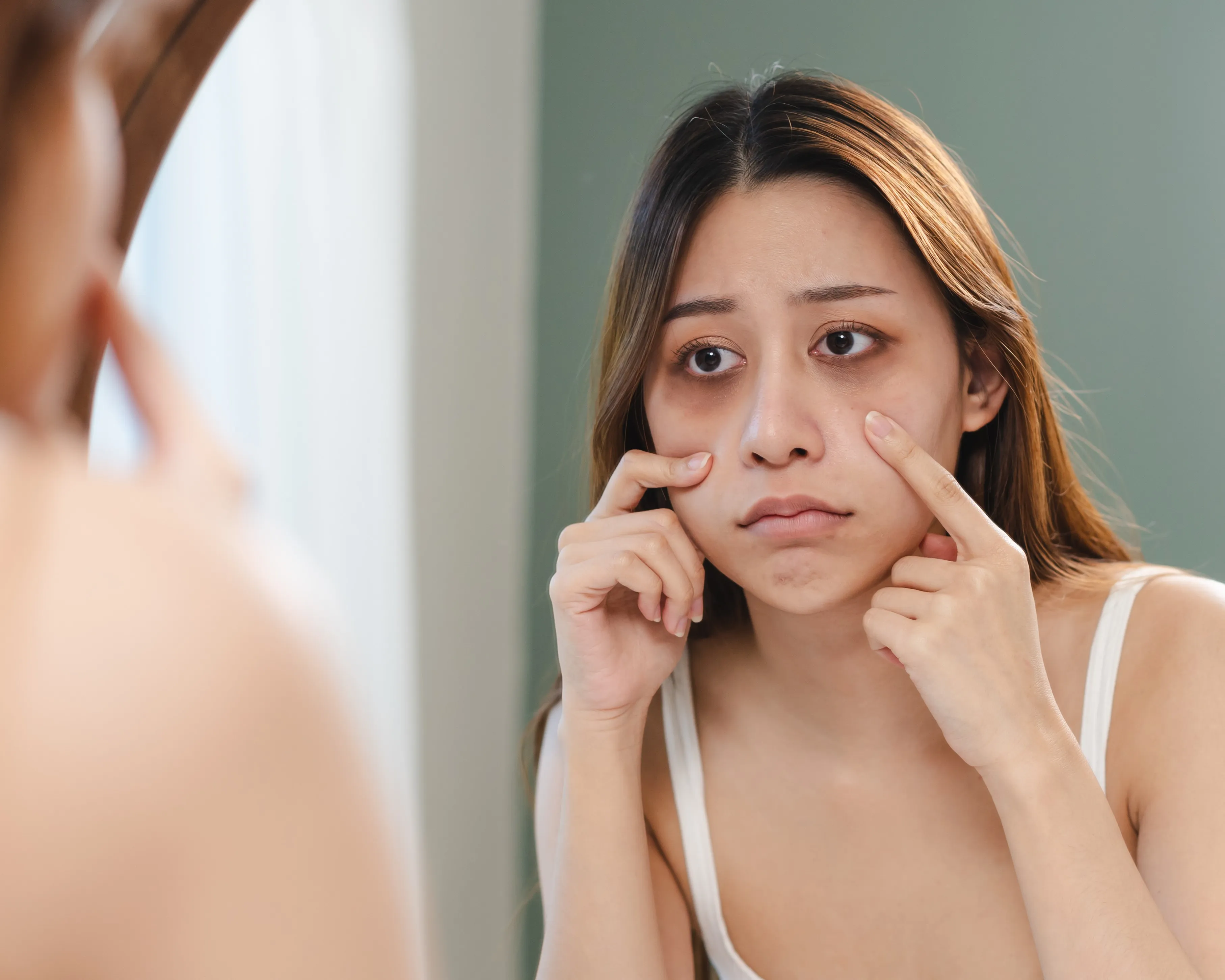 Frau mit Augenringen blickt in den Spiegel